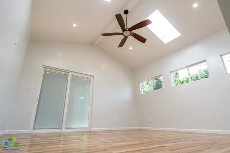 A bright, newly remodeled room addition in Northridge featuring light hardwood floors, a vaulted ceiling with a wooden ceiling fan, recessed lighting, and a large skylight.