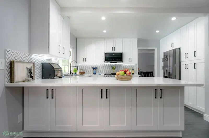 A modern kitchen remodel by Green Star Remodeling in Santa Clarita featuring white shaker-style cabinets, a white marble island, a herringbone tile backsplash, and stainless steel appliances.