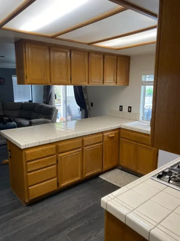 A kitchen featuring honey oak wood cabinets, a white square tile countertop with a matching backsplash, and a built-in sink under a window.