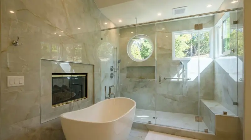 Luxurious bathroom with a glass-enclosed walk-in shower, freestanding tub, double-sided fireplace, and circular accent window.