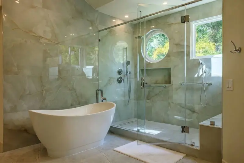 Primary bathroom suite featuring a freestanding white soaking tub, a frameless glass walk-in shower, and marble-look wall tiles.